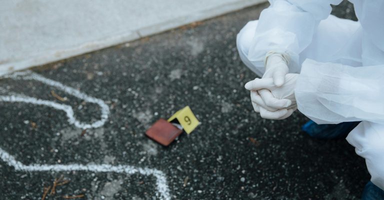 Forensic investigator examines crime scene outline on asphalt in protective suit.