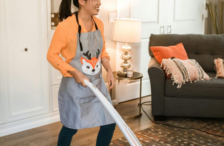 Smiling woman vacuuming a carpet in a cozy living room setting, wearing a festive apron.